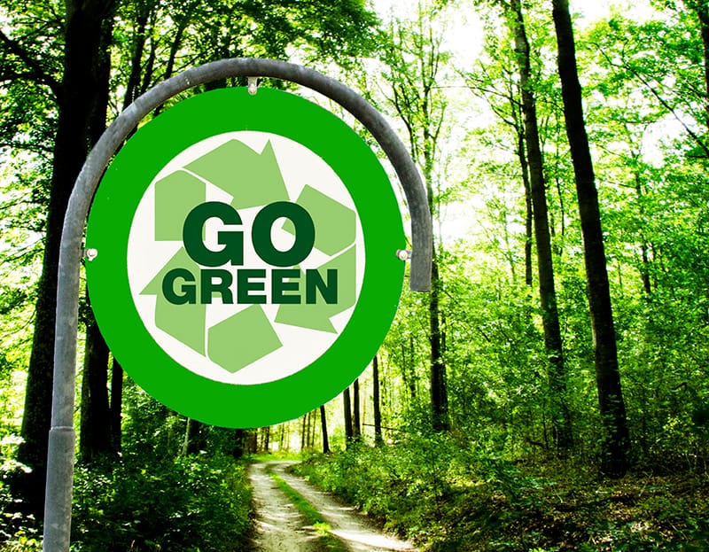 A green sign that says go green in front of trees.